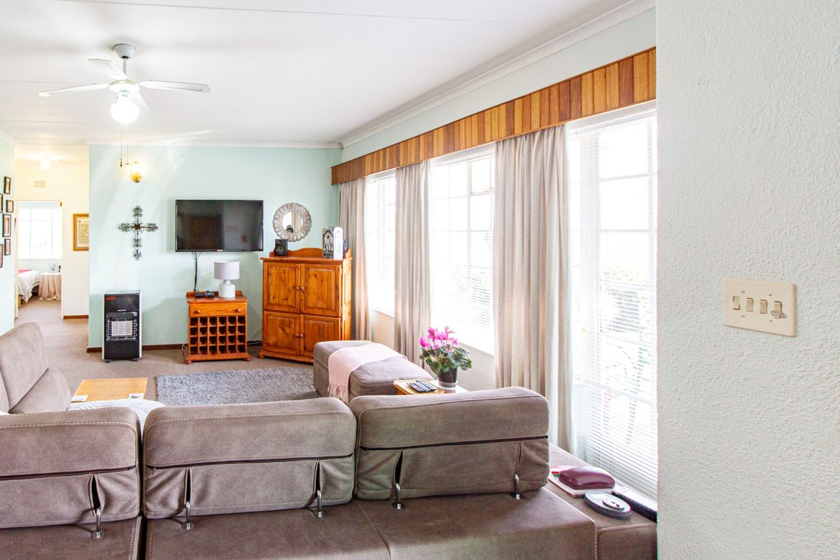 A spacious living room featuring large windows with wooden pelmets, a ceiling fan, and neutral wall finishes.