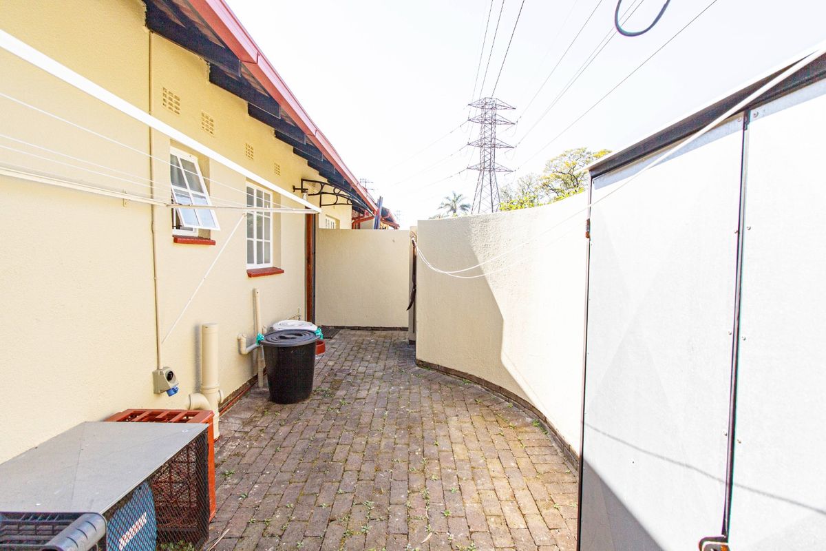 A paved side courtyard area featuring a brick pathway, exterior wall access, and a wall-mounted clothesline.