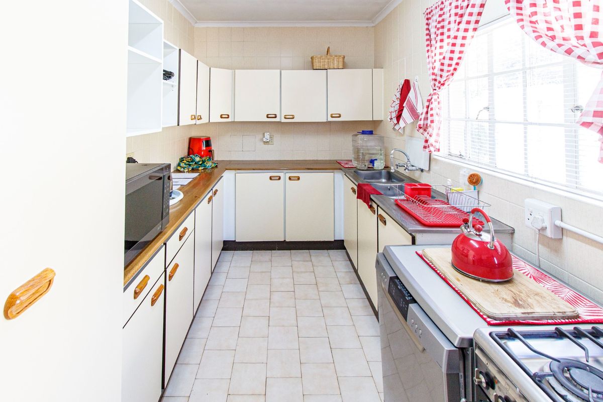 A functional galley-style kitchen featuring cream-colored cabinetry, tiled splashbacks, and a stainless steel double sink with a window view.