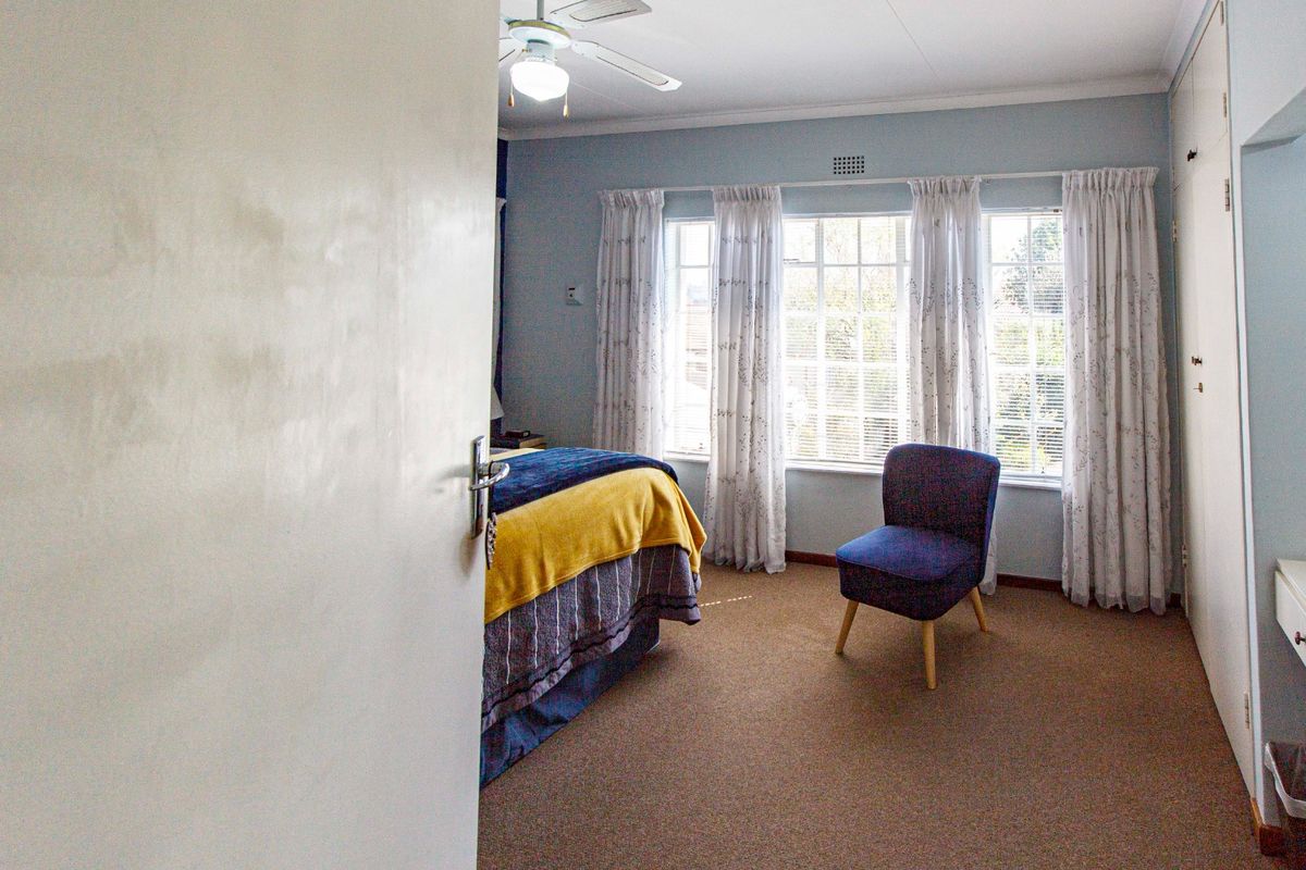 A bedroom featuring built-in cupboards, carpeted flooring, and a ceiling fan, with large windows allowing for natural light.