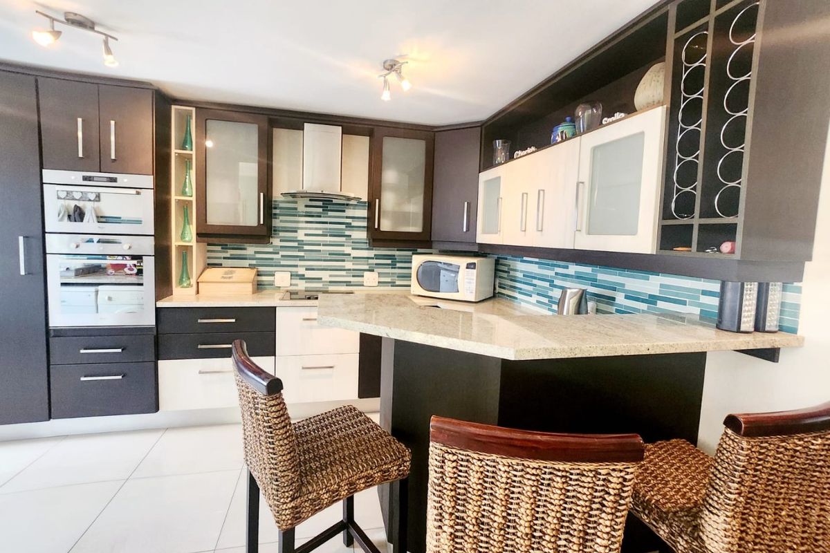 Modern kitchen featuring dark and light cabinetry, granite countertops, a breakfast bar, built-in oven, and a decorative glass tile backsplash.