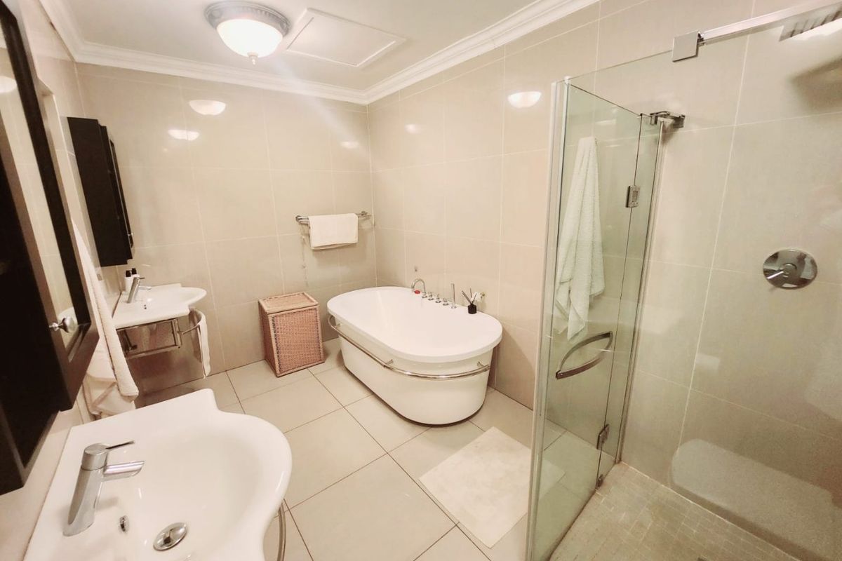 A well-appointed bathroom featuring a freestanding bathtub, a separate glass-enclosed shower, and dual pedestal sinks with neutral wall and floor tiling.