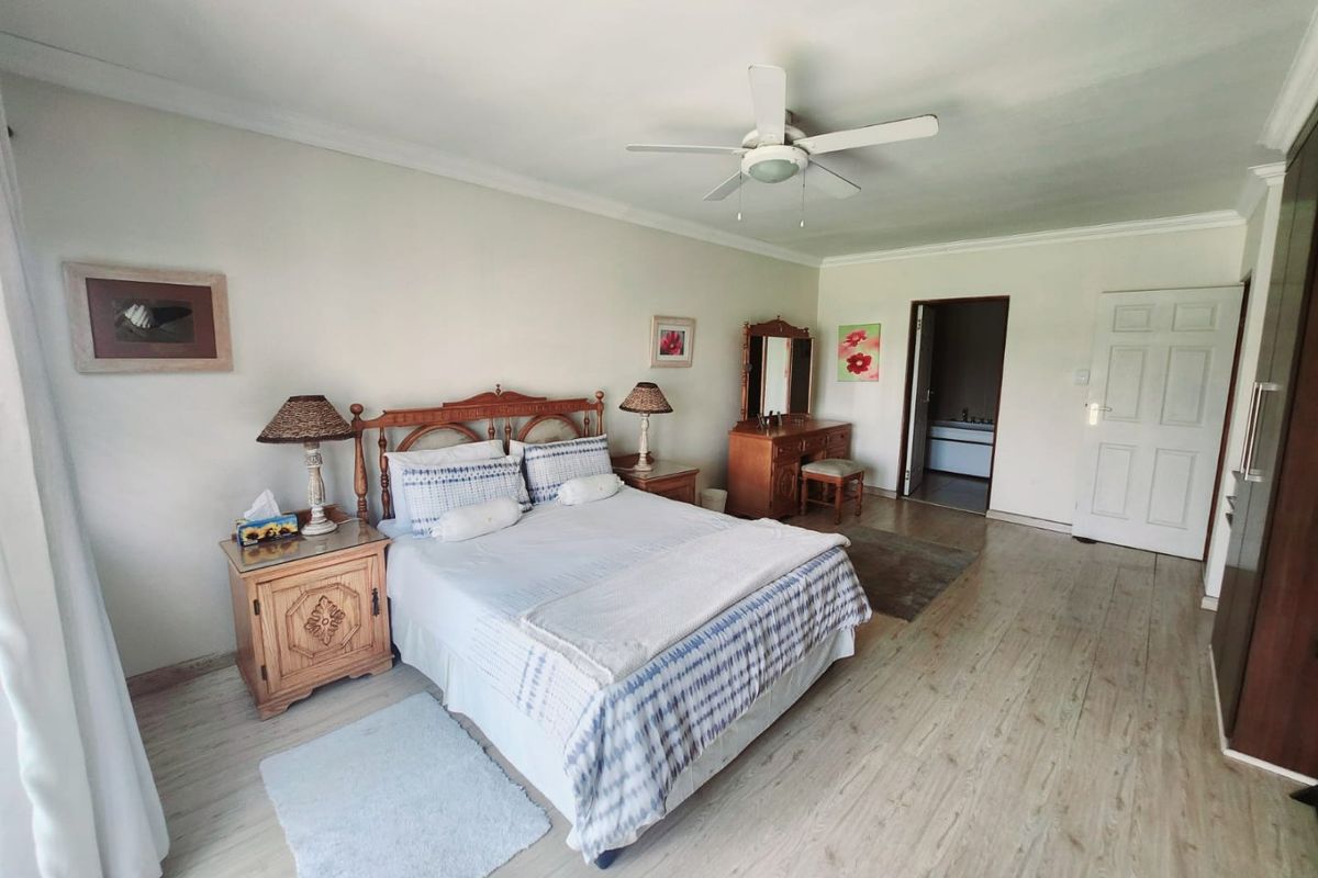 Spacious bedroom featuring light wood-look flooring, a ceiling fan, and direct access to an en-suite bathroom.
