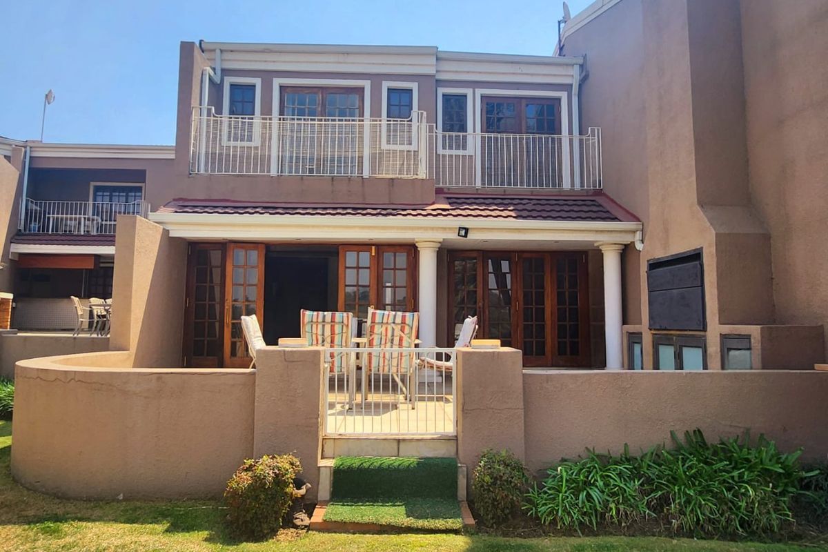 Rear view of a two-story townhouse featuring a ground-floor patio with a built-in braai and an upper-level balcony with metal railings.