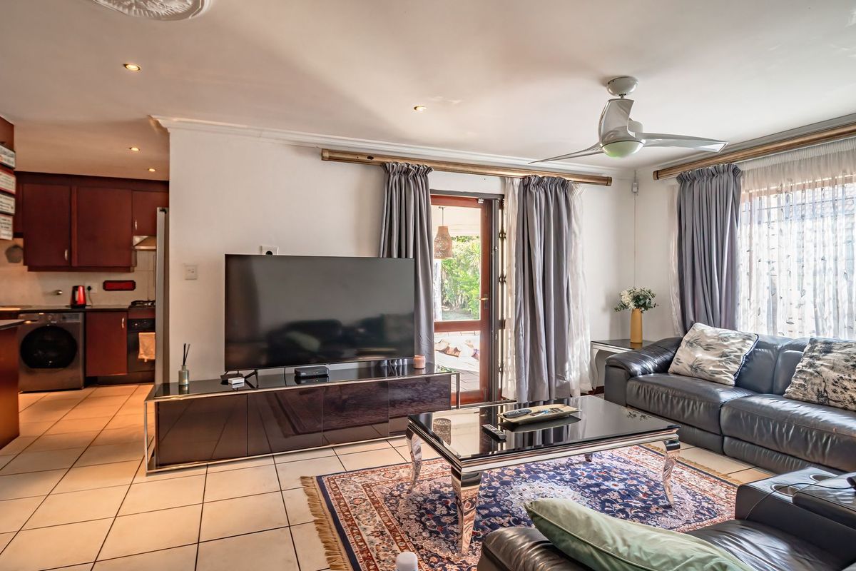 Open-plan living area featuring tiled flooring, a ceiling fan, and direct access to the outdoor patio, seamlessly connected to the adjacent kitchen.