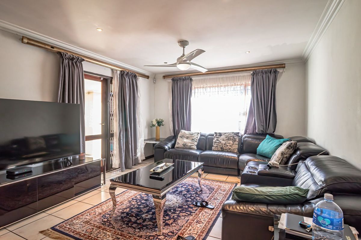 A spacious living room featuring tiled flooring, a ceiling fan, and direct access to an outdoor patio area through a glass door.