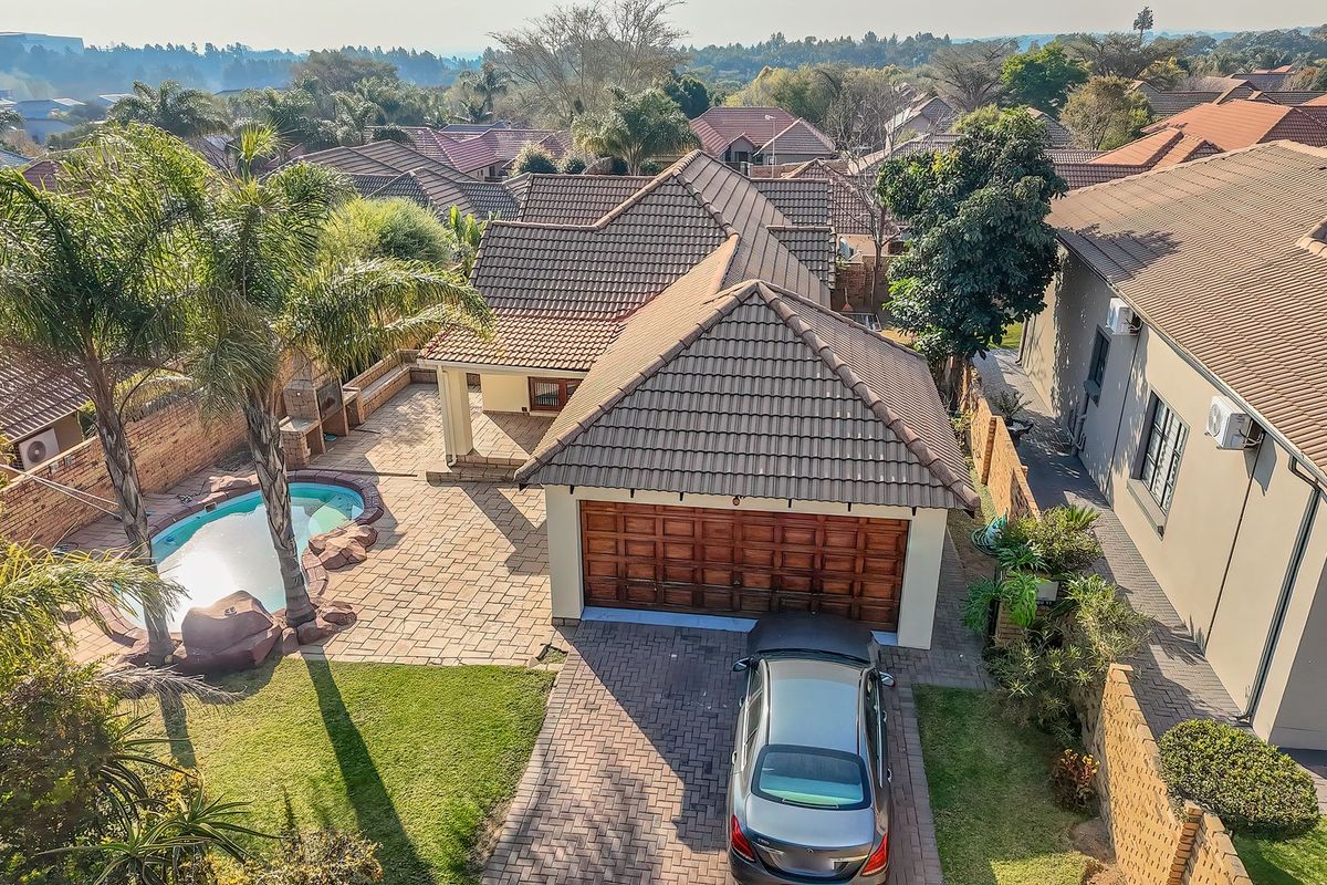 Aerial view of the property featuring a paved driveway, double garage, swimming pool, and a paved patio area within a residential estate setting.