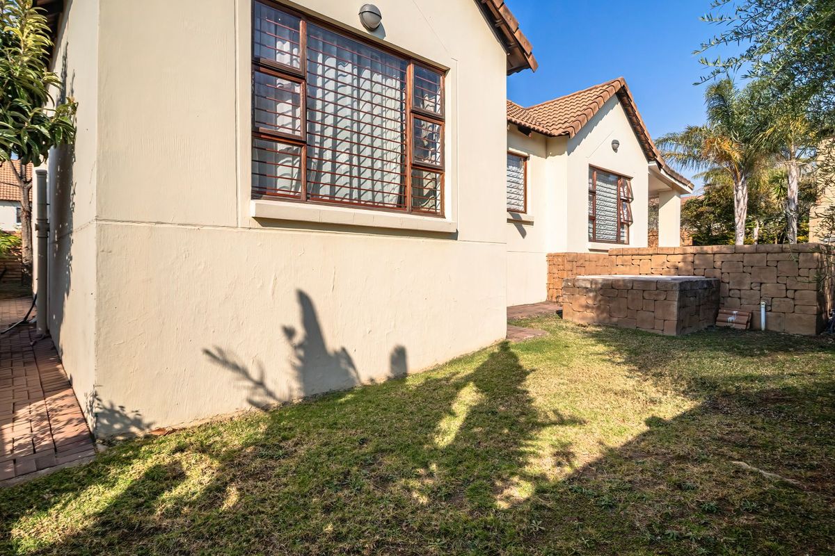 Rear view of the house featuring a paved walkway, lawn area, and a low stone retaining wall.