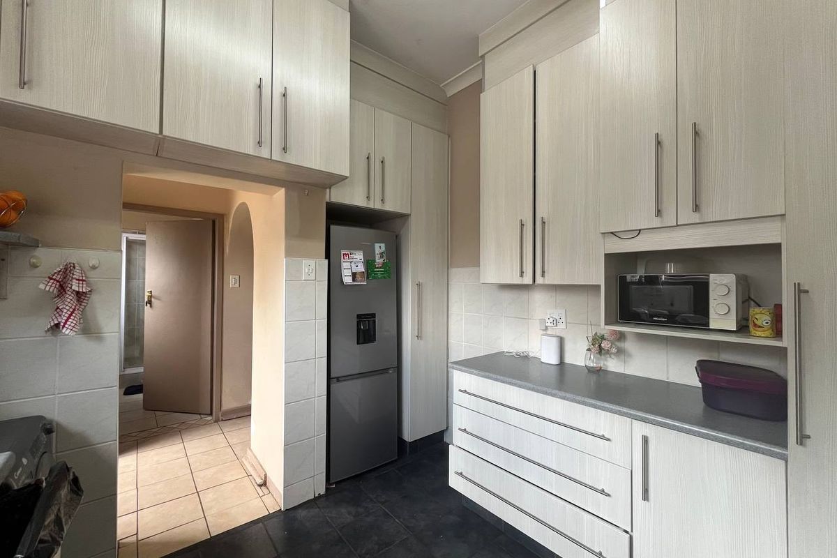 A functional kitchen featuring light wood-grain cabinetry, dark countertops, and tiled flooring, providing ample storage and a practical layout.