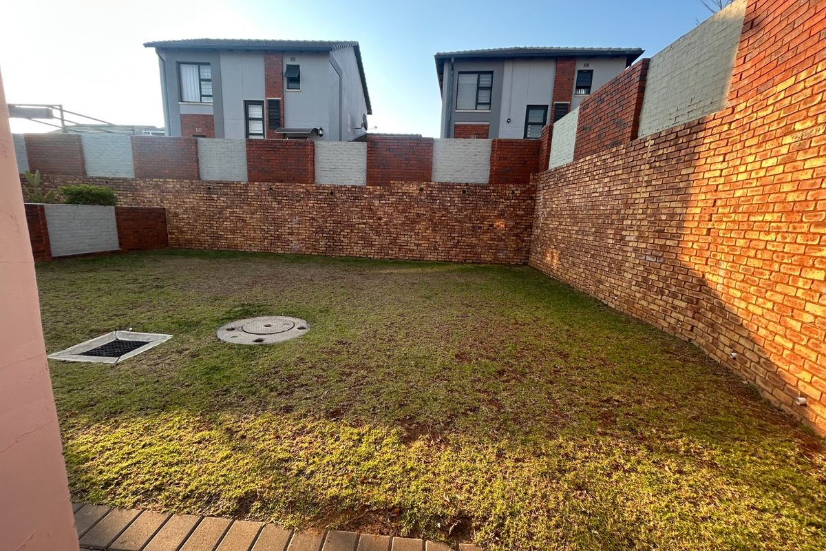 A private rear garden featuring a lawn area enclosed by high perimeter brick boundary walls.