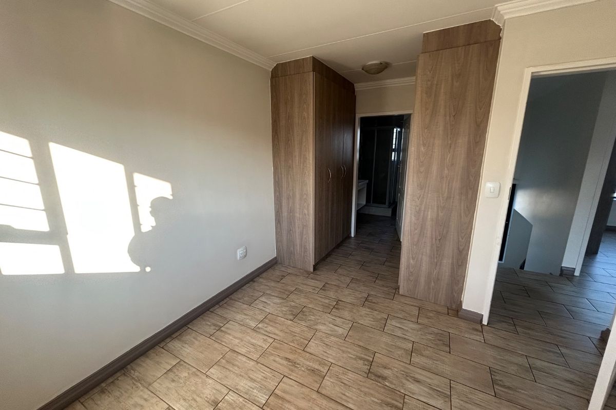 A bedroom featuring wood-look tile flooring and built-in wooden cabinetry, with an adjacent doorway leading to an en-suite bathroom.