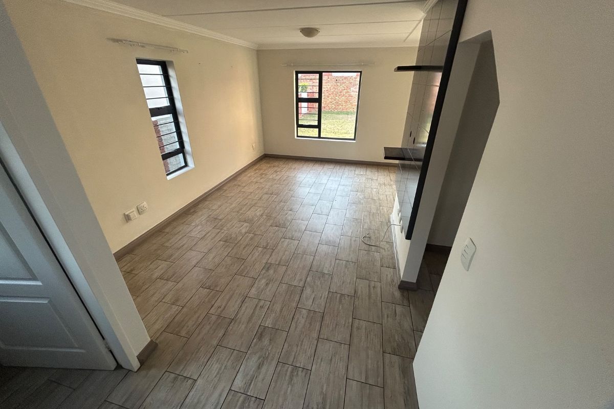 A bright, empty living room featuring wood-look tile flooring, neutral walls, and a built-in feature wall with shelving.