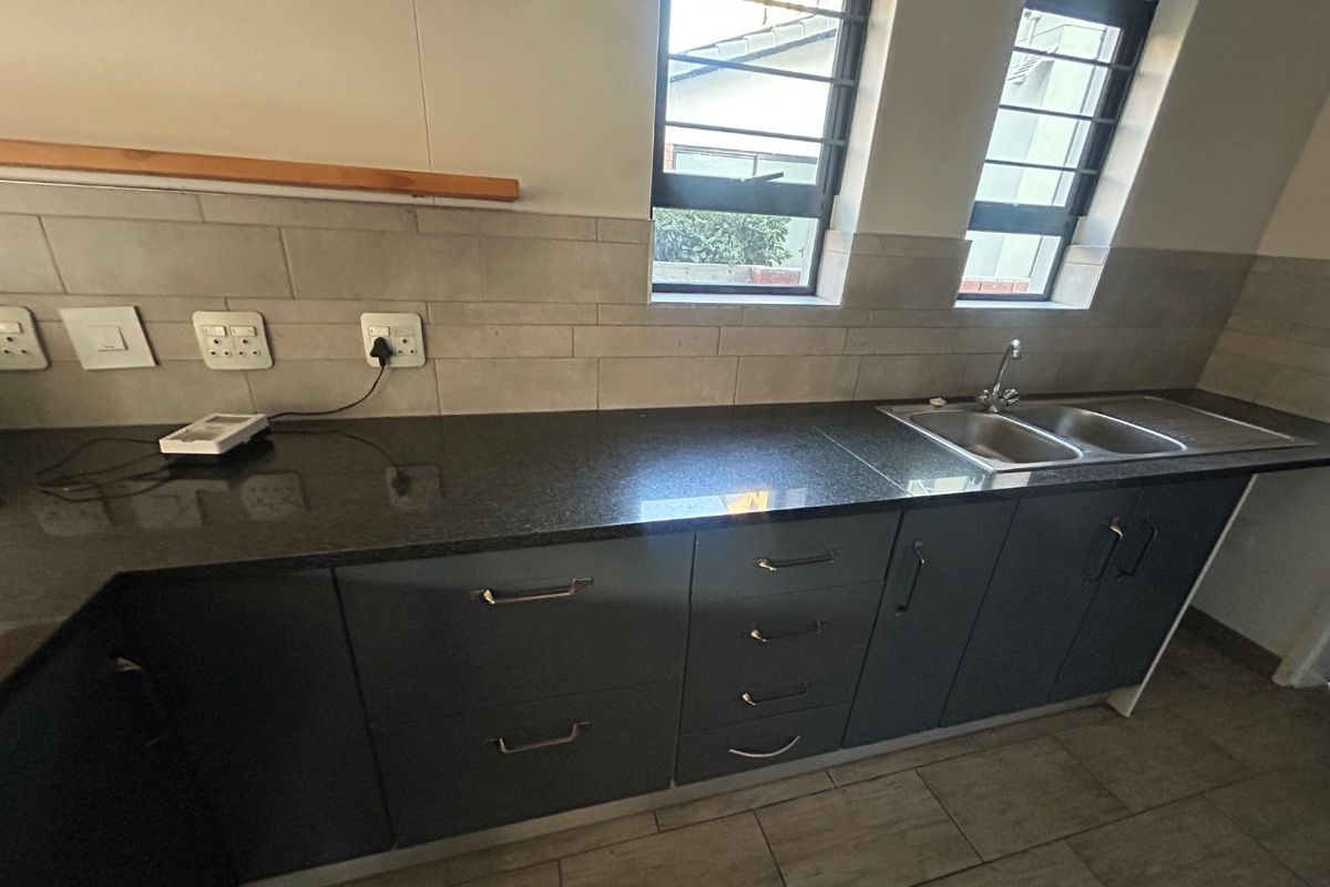 A modern kitchen area featuring dark cabinetry, granite countertops, a double-basin sink, and tiled backsplash with integrated electrical outlets.