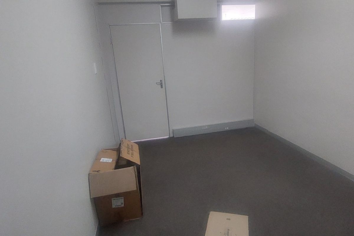 A simple, neutral-toned office space featuring grey carpeting, a single door, and a small high-level window, suitable for a professional workspace.