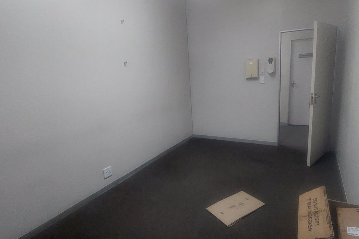A vacant commercial office space featuring neutral walls, dark carpeting, and a single doorway leading to an adjacent area.