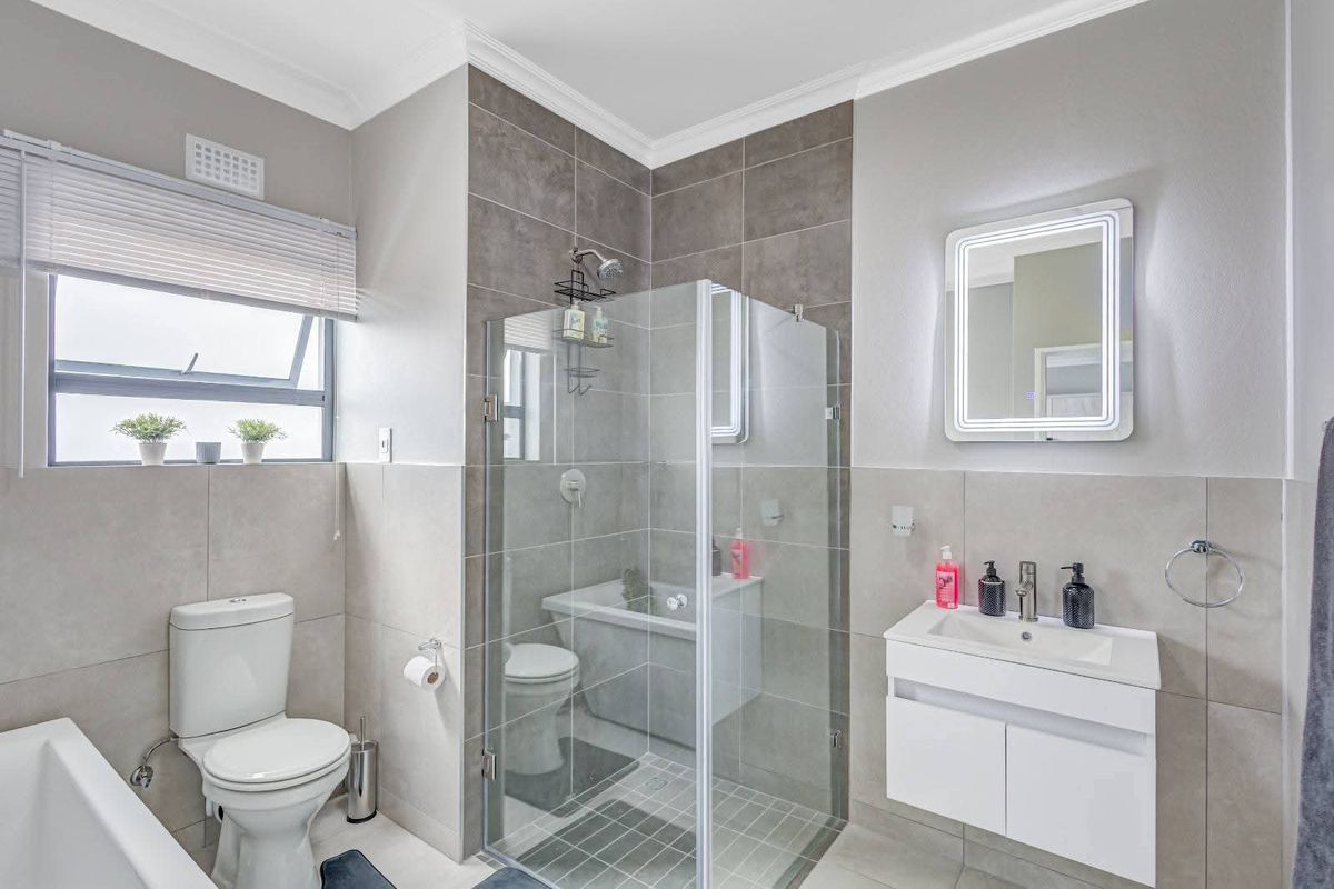 Modern bathroom featuring a glass-enclosed shower, wall-mounted vanity with basin, illuminated mirror, and neutral floor-to-ceiling tiling.