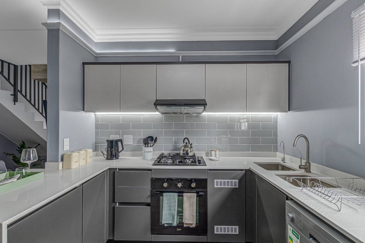 Modern kitchen featuring grey cabinetry, subway tile backsplash, stone countertops, built-in gas hob, oven, and extractor fan with under-cabinet lighting.