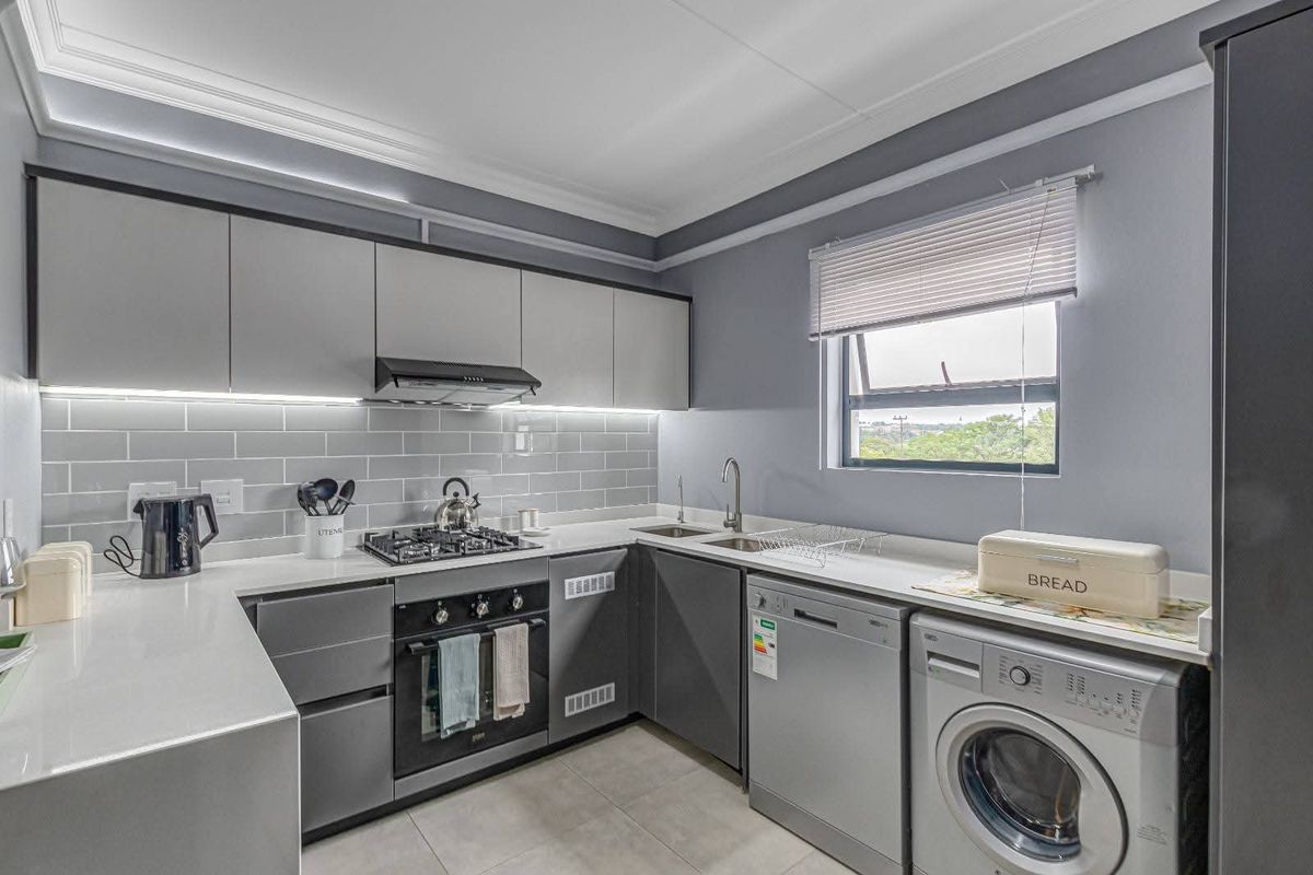 Modern kitchen featuring grey cabinetry, stone countertops, subway tile backsplash, built-in gas hob, oven, extractor fan, and integrated plumbing for appliances.