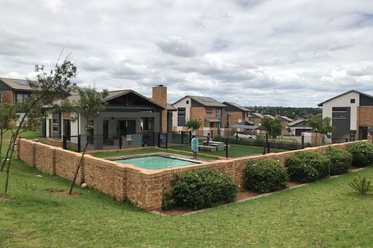 A rear view of a townhouse featuring a private swimming pool, a brick boundary wall, and a covered patio area within a residential estate.