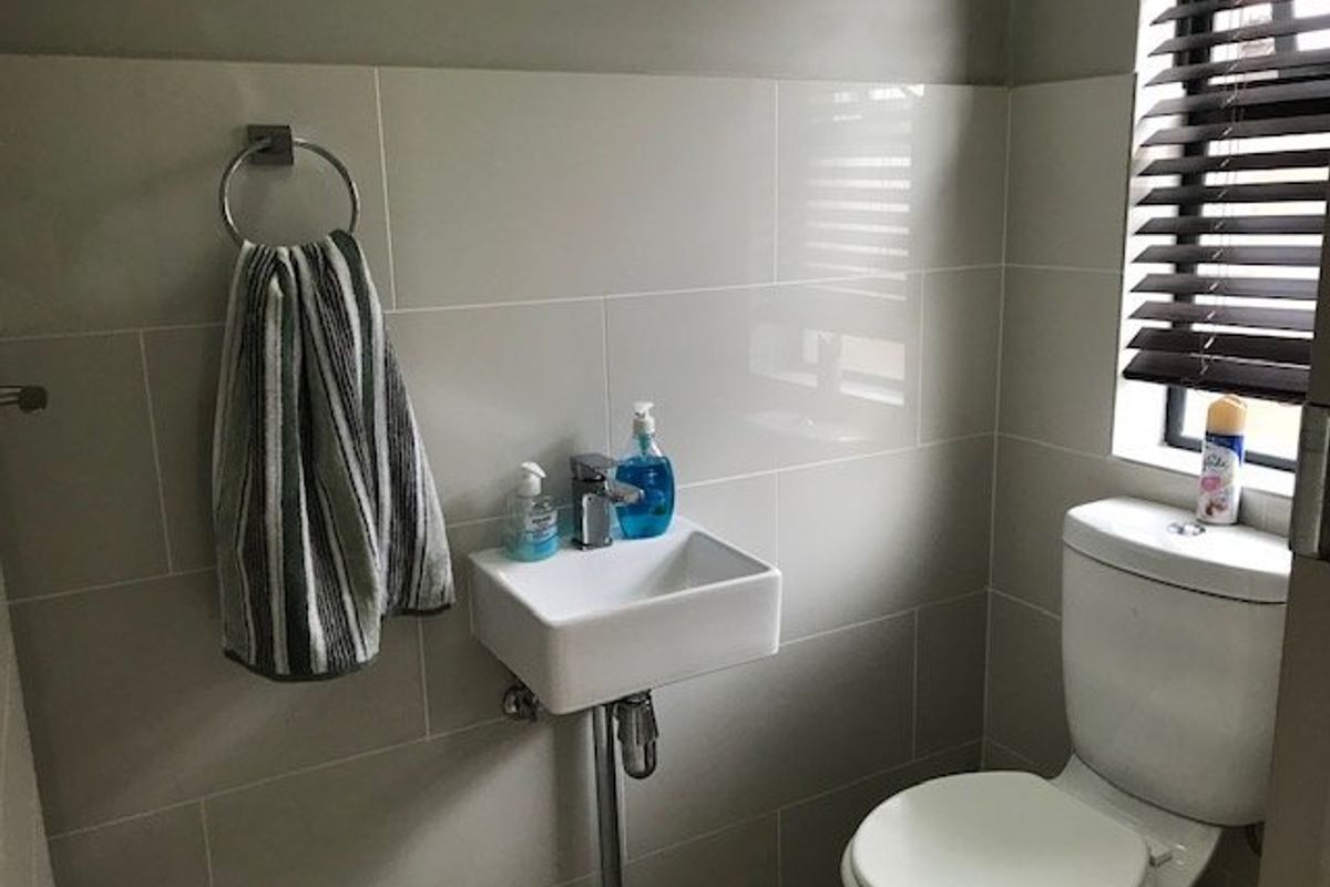 A compact guest bathroom featuring modern wall tiling, a wall-mounted basin with chrome fixtures, and a standard toilet.