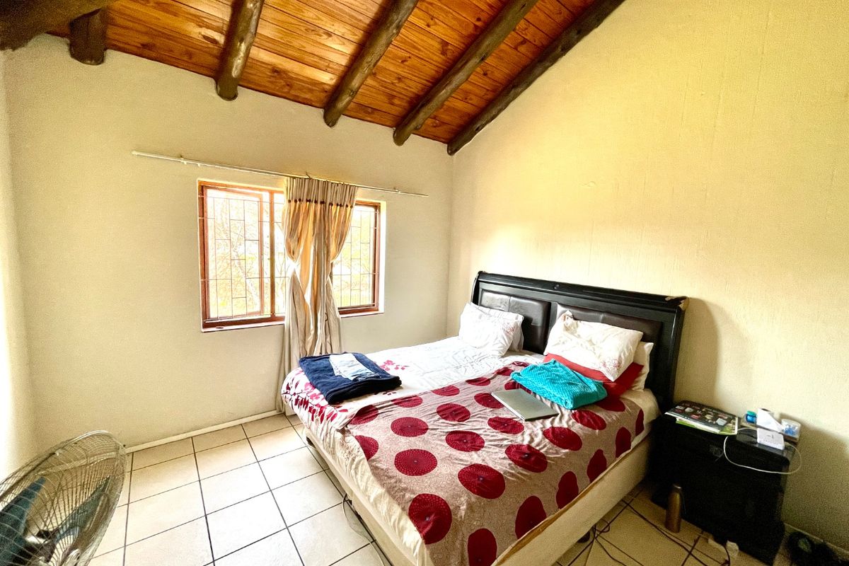 A bedroom featuring a vaulted timber-beamed ceiling, tiled flooring, and a window with security bars.