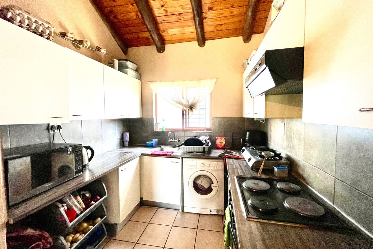 Compact kitchen featuring wooden beamed ceilings, tiled flooring, built-in cabinetry, integrated hob, extractor fan, and under-counter space for a washing machine.