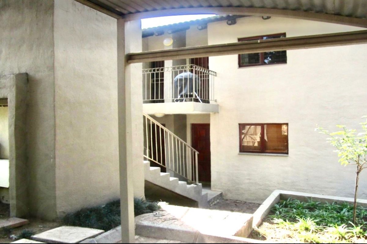 Exterior view of an apartment building featuring a covered walkway, staircase, and balcony with metal railings.