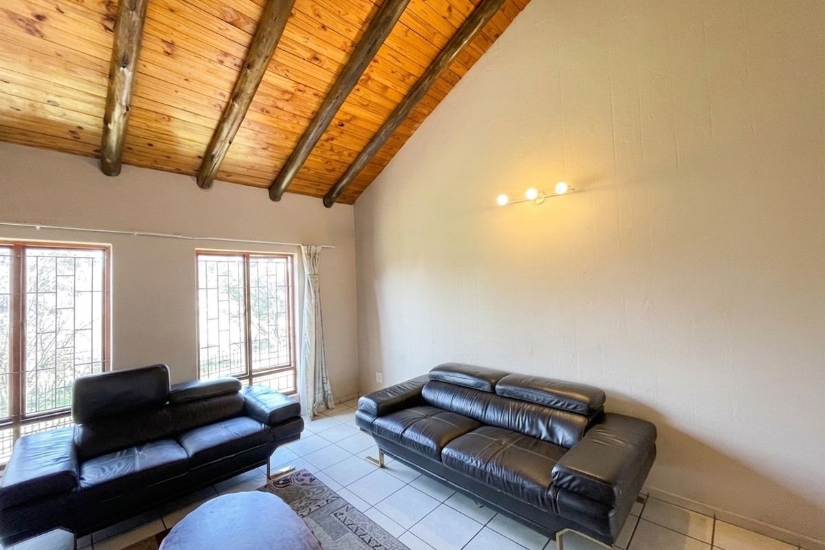 Spacious living room featuring a high vaulted timber-beamed ceiling, tiled flooring, and large windows with security bars.