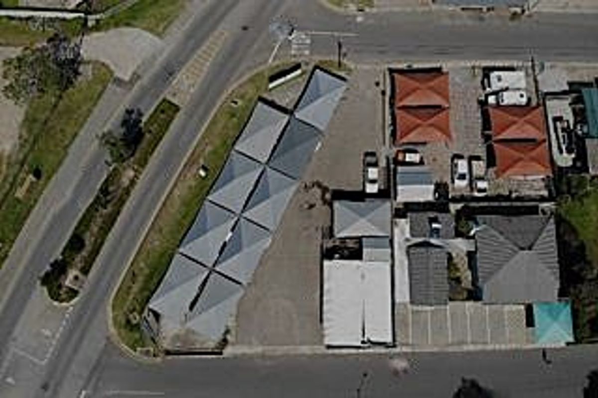Aerial view of a commercial property featuring multiple shade-net parking structures and paved access areas situated on a corner lot.