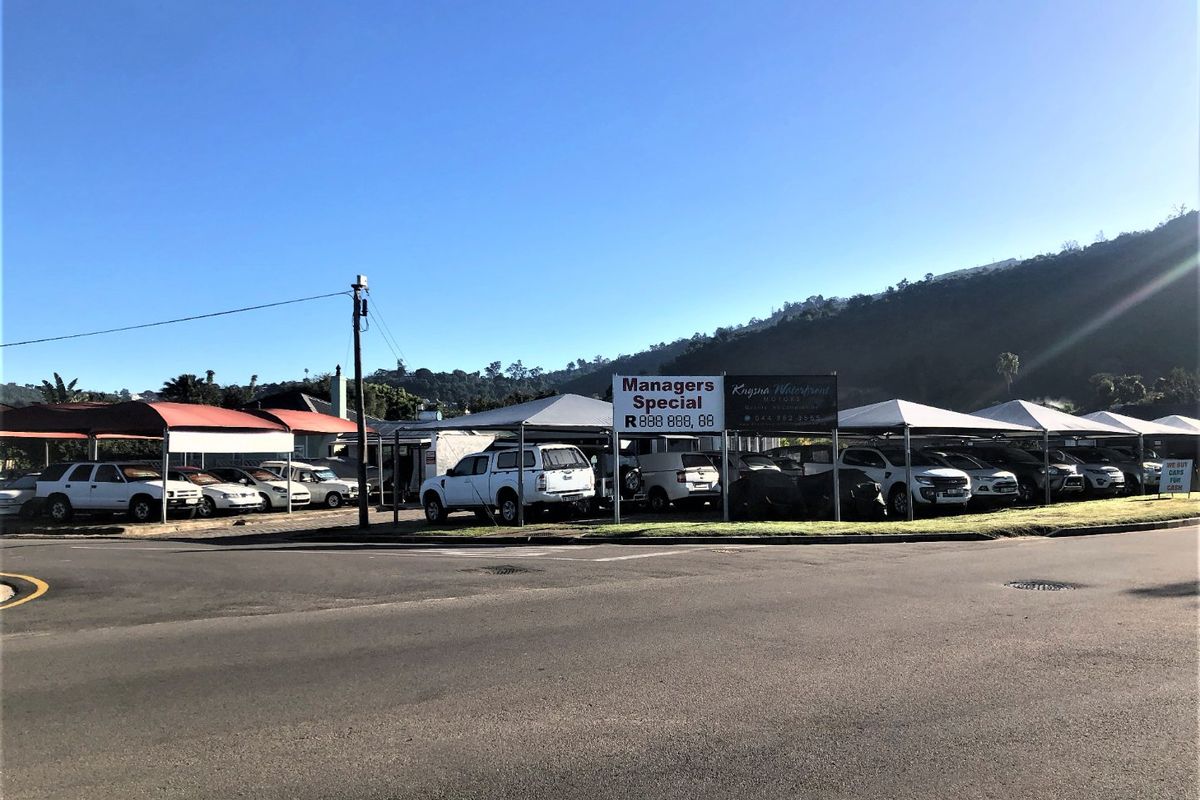 Commercial vehicle display lot featuring multiple covered parking bays and prominent signage, situated on a corner plot with street access.