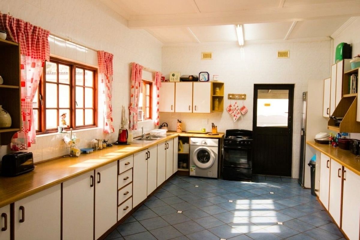 A functional kitchen featuring white cabinetry, laminate countertops, tiled splashbacks, and integrated laundry facilities with direct access to the exterior.