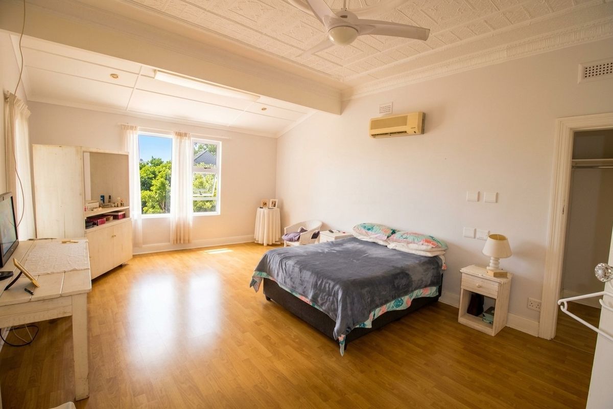 Spacious bedroom featuring timber flooring, a decorative pressed metal ceiling, ceiling fan, and a wall-mounted split system air conditioner.