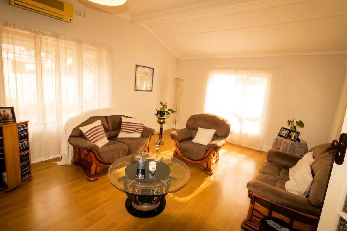 A bright living room featuring laminate flooring, a vaulted ceiling, and a wall-mounted split-system air conditioner.