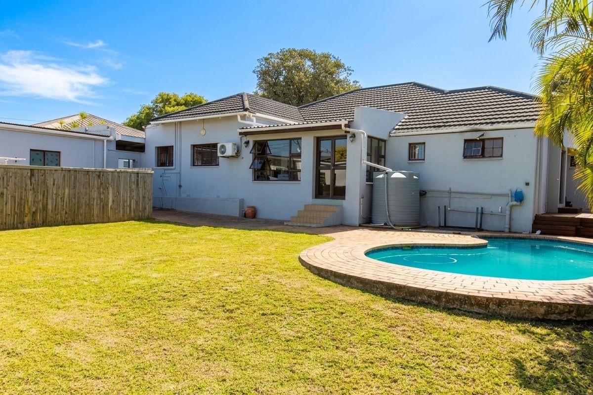 Rear view of the property featuring a swimming pool, paved surround, water tank, and a well-maintained lawn area.