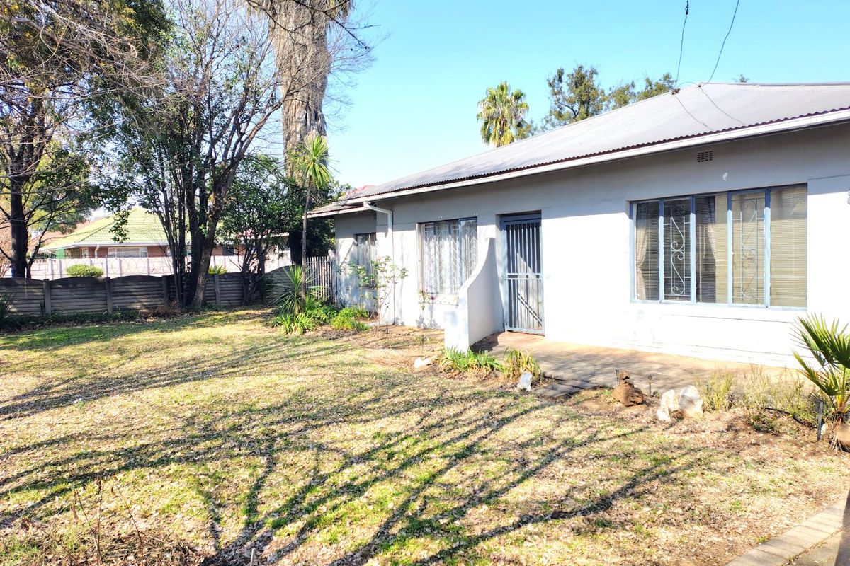 A view of the rear exterior of the house, featuring a paved patio area and a spacious garden with mature trees.