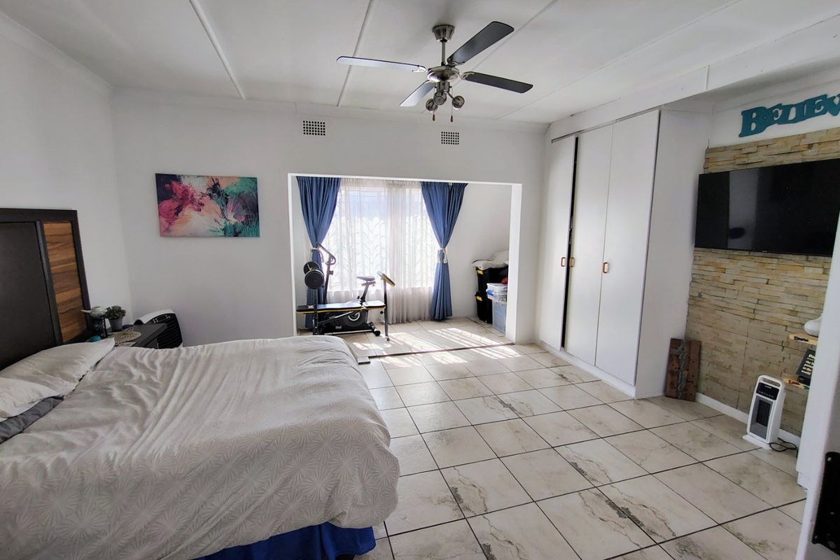 Spacious bedroom featuring large format floor tiles, built-in cupboards, a ceiling fan, and an adjoining sunroom or alcove area.