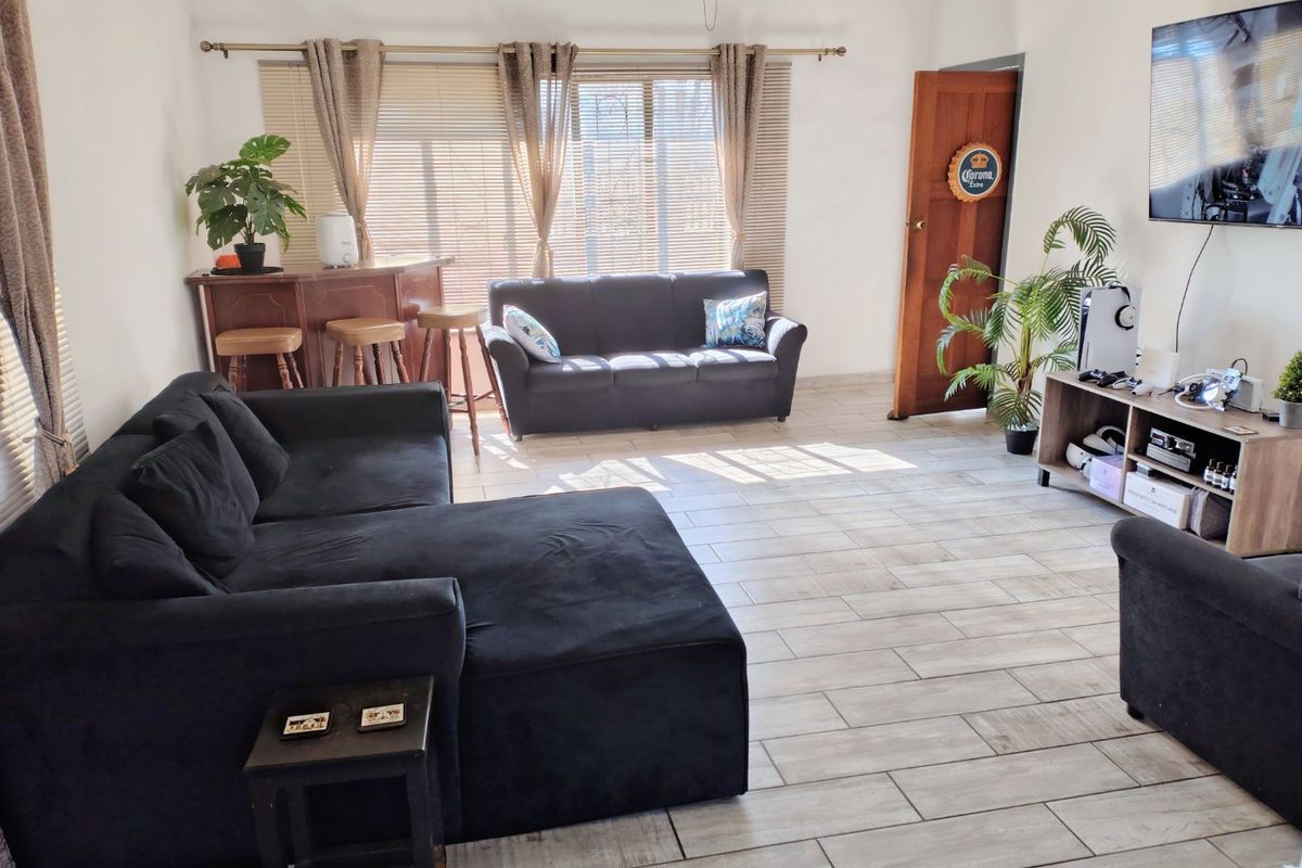 Spacious living room featuring light-toned wood-look floor tiles, large windows with blinds, and a solid timber door.