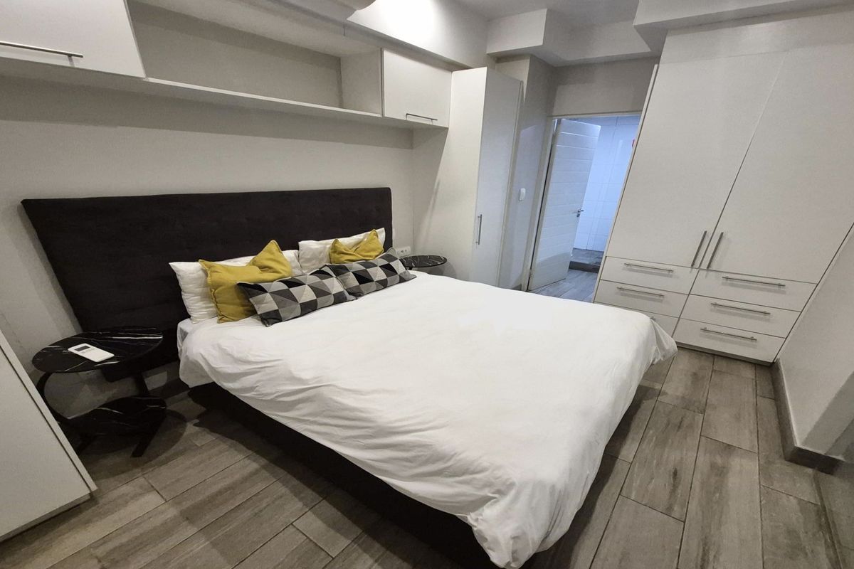 A well-maintained bedroom featuring built-in white cabinetry, overhead shelving, and wood-look tiled flooring, with an adjoining en-suite bathroom.