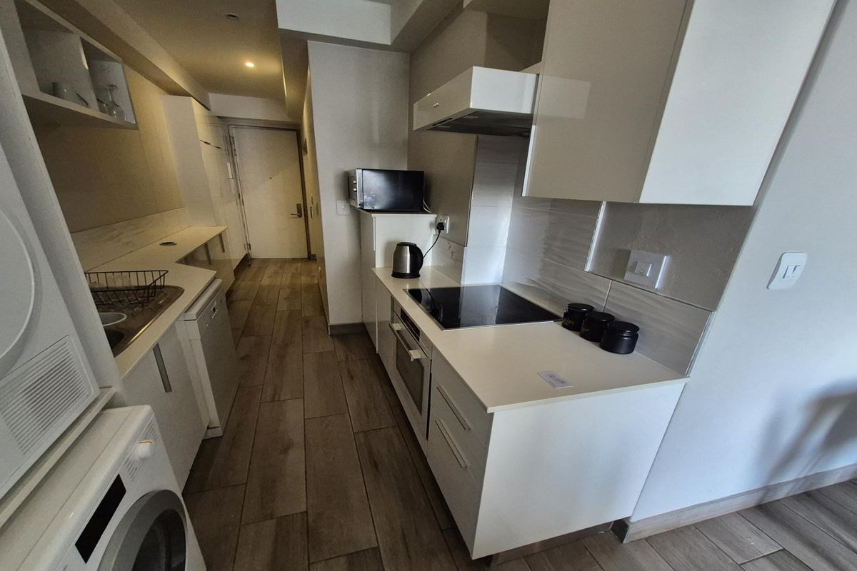 Modern compact kitchen featuring white cabinetry, integrated oven, electric hob, extractor fan, and dedicated space for laundry appliances.