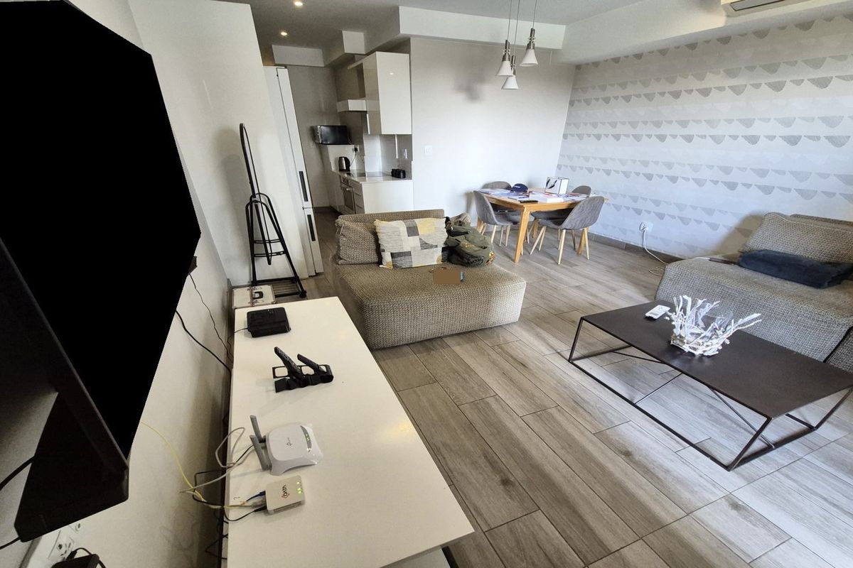 Open-plan living area featuring wood-look tile flooring, a modern kitchen with white cabinetry, and a dining space, creating a bright and functional layout.