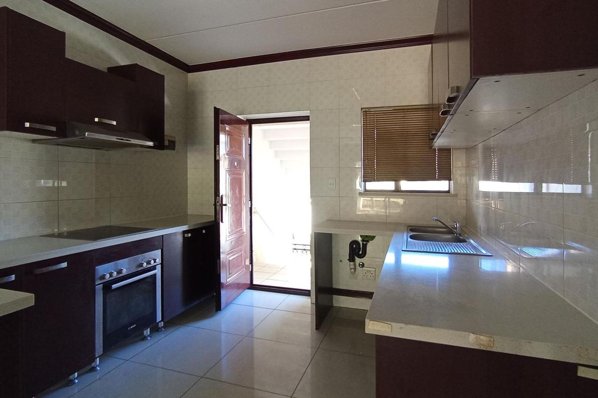 A functional kitchen featuring dark cabinetry, built-in oven, extractor fan, and tiled surfaces with direct access to an exterior doorway.