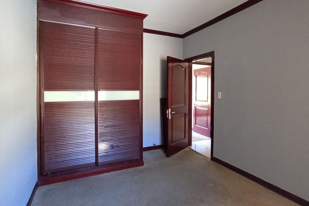 A bedroom featuring built-in wooden sliding door cupboards, neutral wall finishes, and carpeted flooring, providing a functional and clean living space.