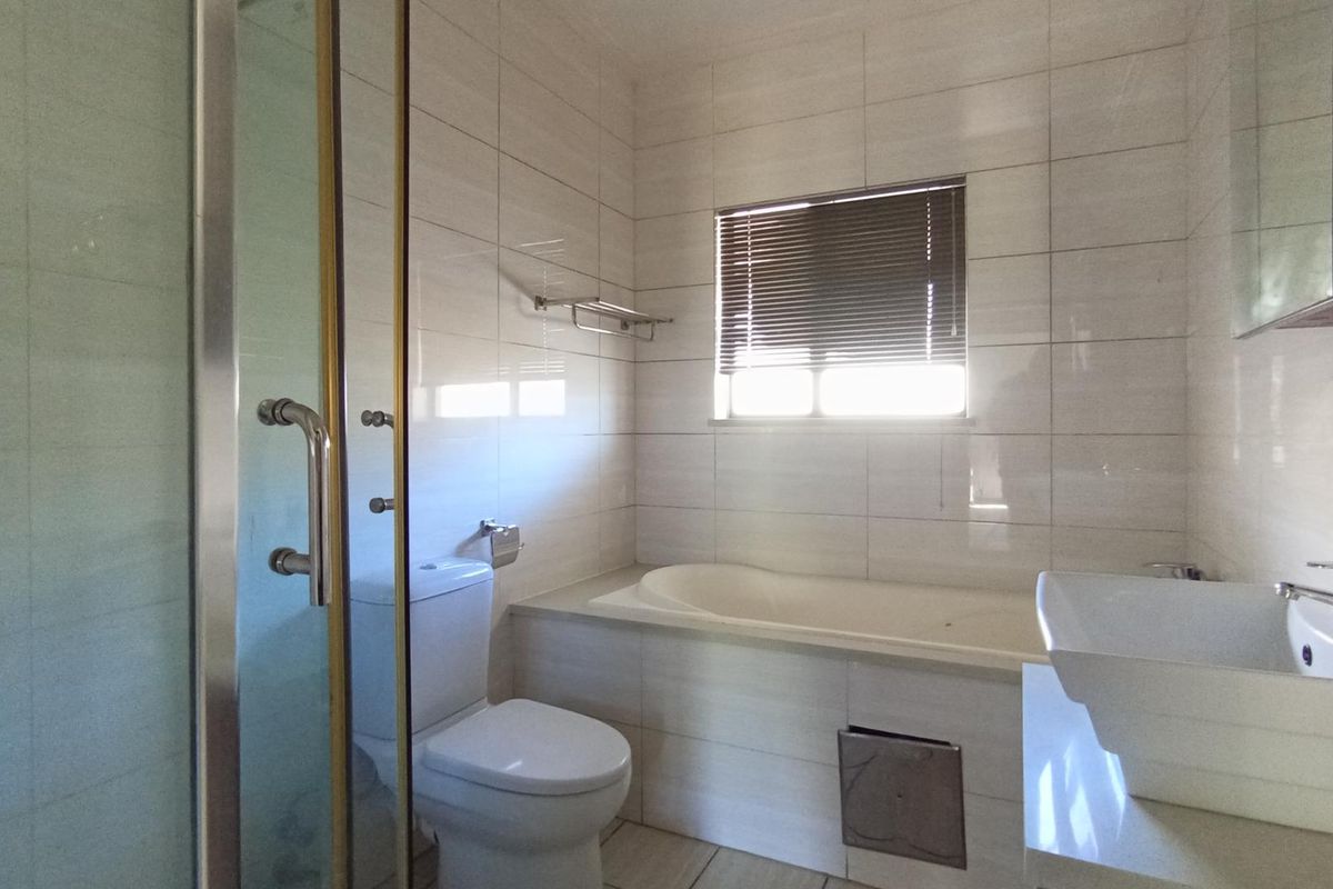 A functional bathroom featuring a built-in bathtub, separate glass-enclosed shower, wall-mounted basin, and tiled walls.