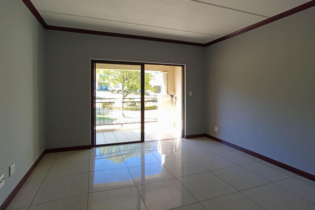 A bright, empty living room featuring tiled flooring, dark crown molding, and sliding glass doors that open onto a private balcony.