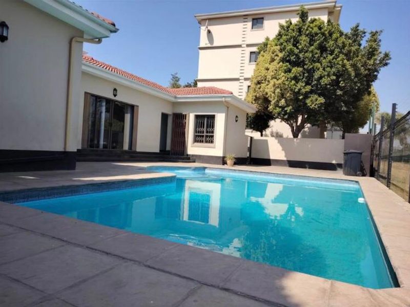 A well-maintained outdoor swimming pool area featuring a tiled surround, adjacent to the main building structure with sliding door access.