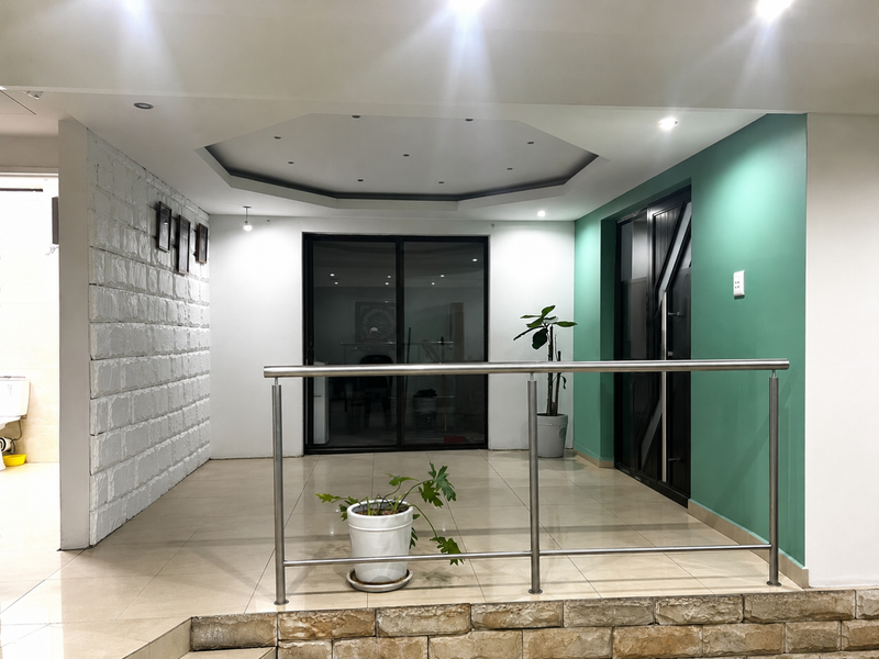 A spacious interior landing area featuring a raised tiled platform, stainless steel balustrade, recessed ceiling lighting, and a decorative stone-clad feature wall.