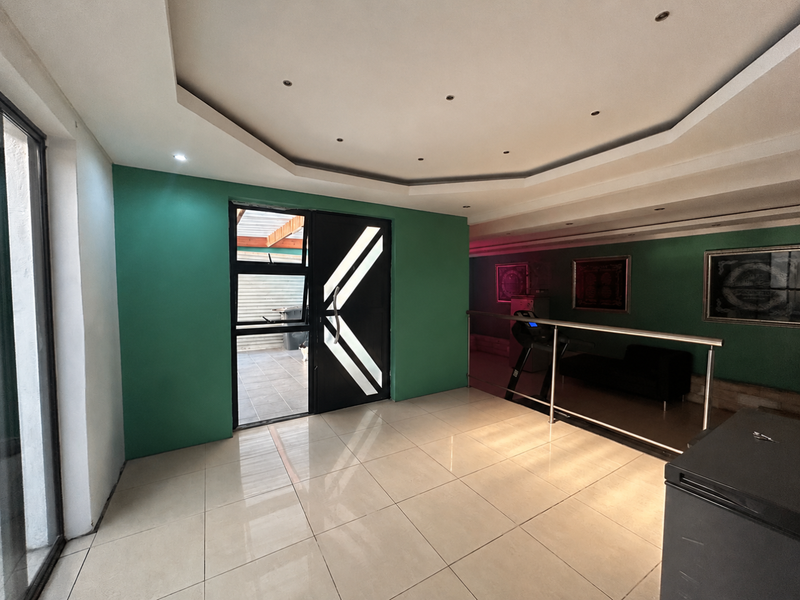 An open-plan living area featuring a modern geometric door, recessed tray ceiling with downlights, and a metal balustrade overlooking a lower level.