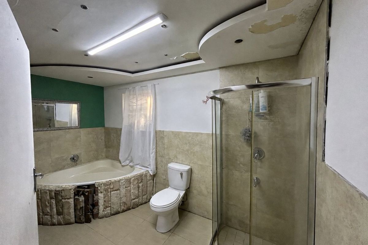 A dated bathroom featuring a corner bathtub with stone-style cladding, a separate glass shower enclosure, and a standard toilet.