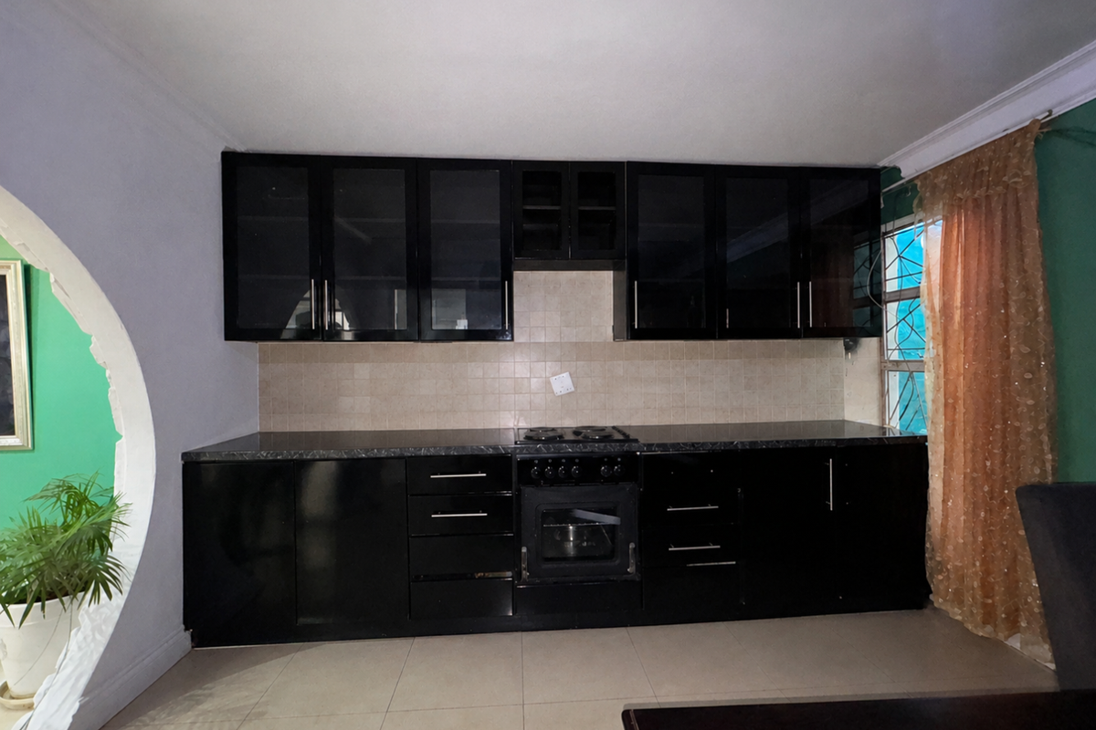 A kitchen featuring black cabinetry, integrated oven and hob, tiled backsplash, and tiled flooring, with a distinctive arched architectural detail.