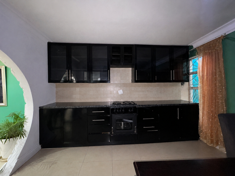 A kitchen featuring black cabinetry, integrated oven and hob, tiled backsplash, and tiled flooring, with a distinctive arched architectural detail.
